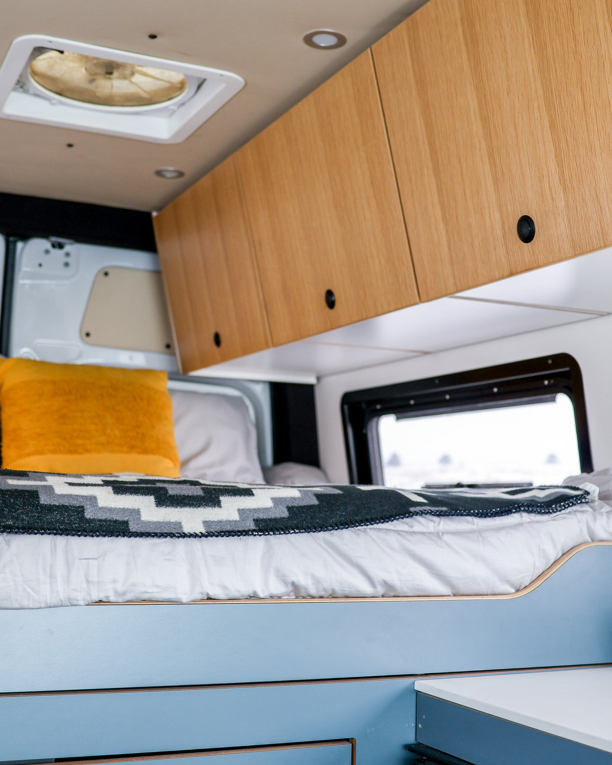 Featherbuilt upper cabinets above the bed in a Sprinter van